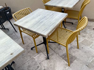 des chaises et des tables jaunes sur une terrasse, avec une plante en pot en arrière-plan