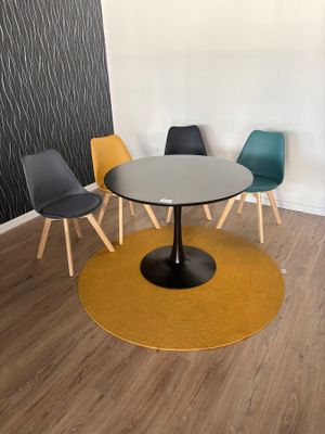 Des chaises aux couleurs vives sont disposées autour d'une table ronde dans une pièce