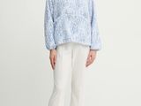 a woman standing in front of a white background wearing a blue sweater and white pants