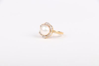 une bague en perle blanche et diamants posée sur une surface blanche