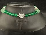 a green beaded necklace with a cross charm on a mannequin