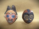 two wooden masks are sitting on a gold surface