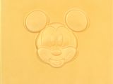 un visage de Mickey Mouse sur un morceau de fromage posé sur une surface blanche