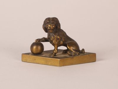 statue en bronze représentant un lion tenant une boule, posée sur un socle en marbre