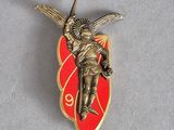 une photo d'une broche rouge et dorée représentant un ange tenant une épée