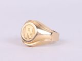 une image représentant une bague chevalière en or sur laquelle figure la lettre « r »