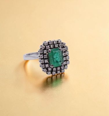 un gros plan d'une bague sertie d'une émeraude et de diamants sur une surface en or