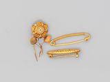 deux épingles à cheveux dorées et une broche en forme de fleur posées sur un fond gris
