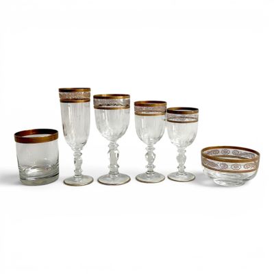 six verres à vin à bord doré sont alignés sur une surface blanche
