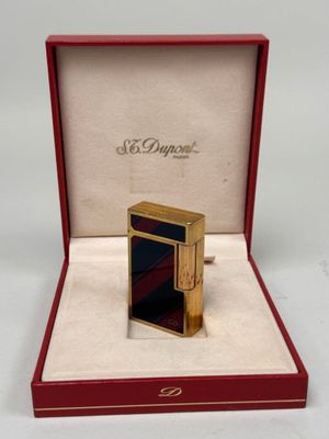 une image représentant un briquet doré dans une boîte rouge ornée d'une bande noire et rouge