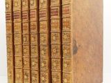 six old books lined up in a row on a white surface