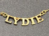 a close up of a gold necklace with the word lyddie on it