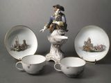 a figurine of a man on a pedestal next to three cups and saucers