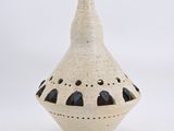 un vase blanc percé de trous, posé sur une surface blanche