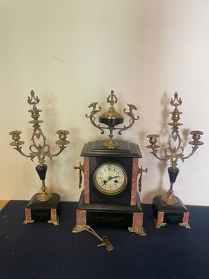 a clock sitting on top of a table next to three candelabs
