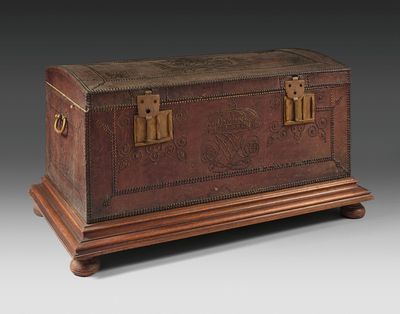 an antique leather trunk with brass hardware on a wooden stand