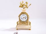 une petite horloge en or surmontée d'un oiseau, à côté d'une paire de ciseaux