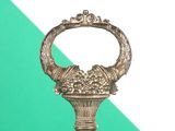 a metal object with a handle on a green and white background