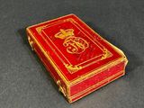 un petit livre rouge aux bords dorés posé sur une surface noire