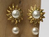 pair of pearl and gold sunburst earrings on a wooden stand