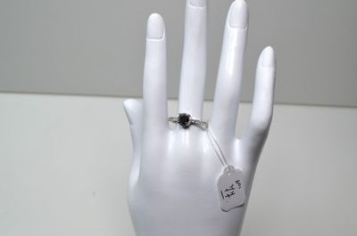 une main de mannequin blanche tenant une bague à laquelle est attachée une étiquette