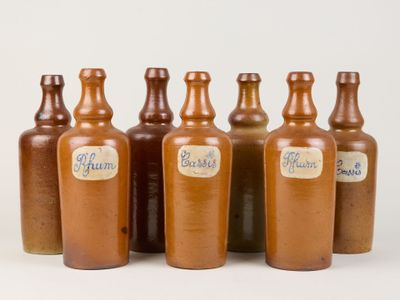 six bouteilles marron munies d'étiquettes sont alignées en rangée