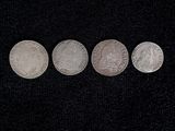 four different types of silver coins on a black surface