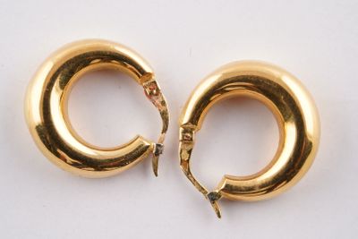 une paire de boucles d'oreilles créoles dorées posées sur un fond blanc