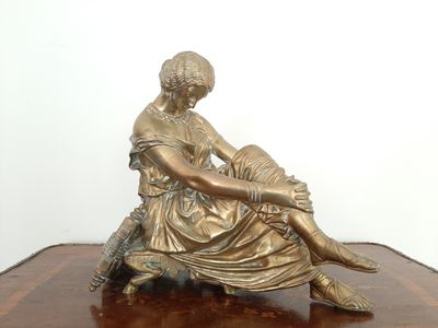 statue en bronze représentant une femme assise sur une table en bois, les jambes croisées