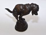 statue en bronze d'un chien sur un socle posé sur une surface blanche
