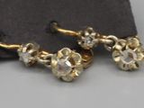 paire de boucles d'oreilles dorées ornées de cristaux transparents, présentées sur un tissu noir