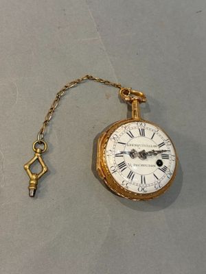 a gold pocket watch with a key hanging from it ' s chain