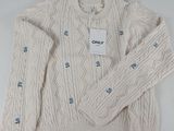 Le pull est blanc et comporte des boutons bleus.