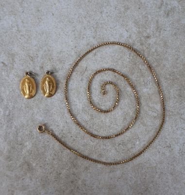 deux colliers en or et une paire de boucles d'oreilles posés sur une surface blanche