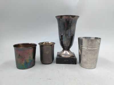 quatre tasses en métal de formes différentes et un vase en argent posés sur une surface blanche