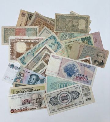 une pile de billets de différentes devises posée sur une surface blanche