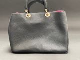 a black handbag with a pink handle on a gray background