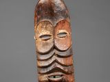 a carved wooden mask with a face on a gray background