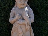 a statue of a boy holding a bird in front of a hedge