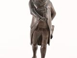 statue en bronze représentant un homme muni d'une canne et portant un chapeau, posée sur un socle