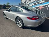 une Porsche 911 argentée garée devant un immeuble, sur un parking