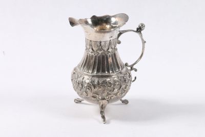 un pichet ancien plaqué argent posé sur un socle, sur fond blanc