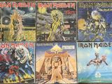 several iron maiden cds are stacked on a wooden table