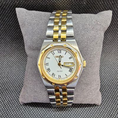une montre en argent et en or posée sur un coussin, sur une table