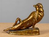 bronze sculpture of a dog laying on its back on a wooden surface
