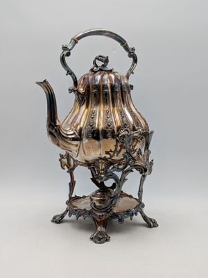 une théière ancienne en argent posée sur un socle, sur fond gris