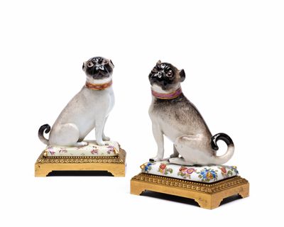 une paire de figurines représentant un carlin et un chat, posées sur un coussin