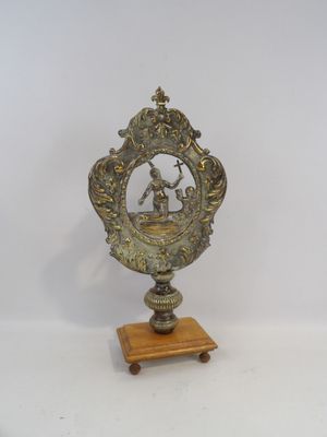 une petite horloge en métal posée sur un socle en bois, elle-même posé sur une surface blanche
