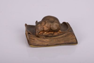 une petite souris en bronze posée sur un livre, sur une surface blanche