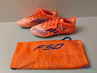 deux paires de chaussures de foot orange posées sur une table à côté d'un sac